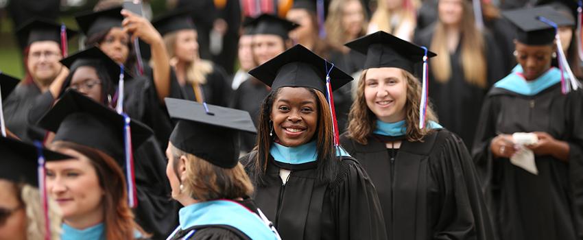 African American Female graduate smiling in cap and gown walking in a line to graduation.