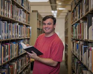 Male student in library holding a book.